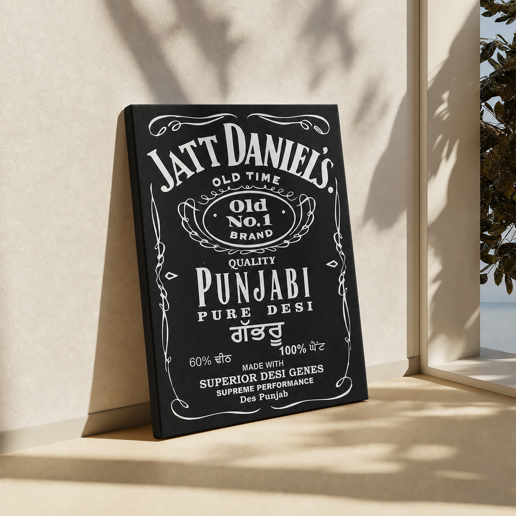 A black rectangular wall art print or sign with white vintage-style text reading 'Jatt Daniel's' and 'Punjabi Pure Desi,' leaning against a beige wall in a sunlit interior near a window.