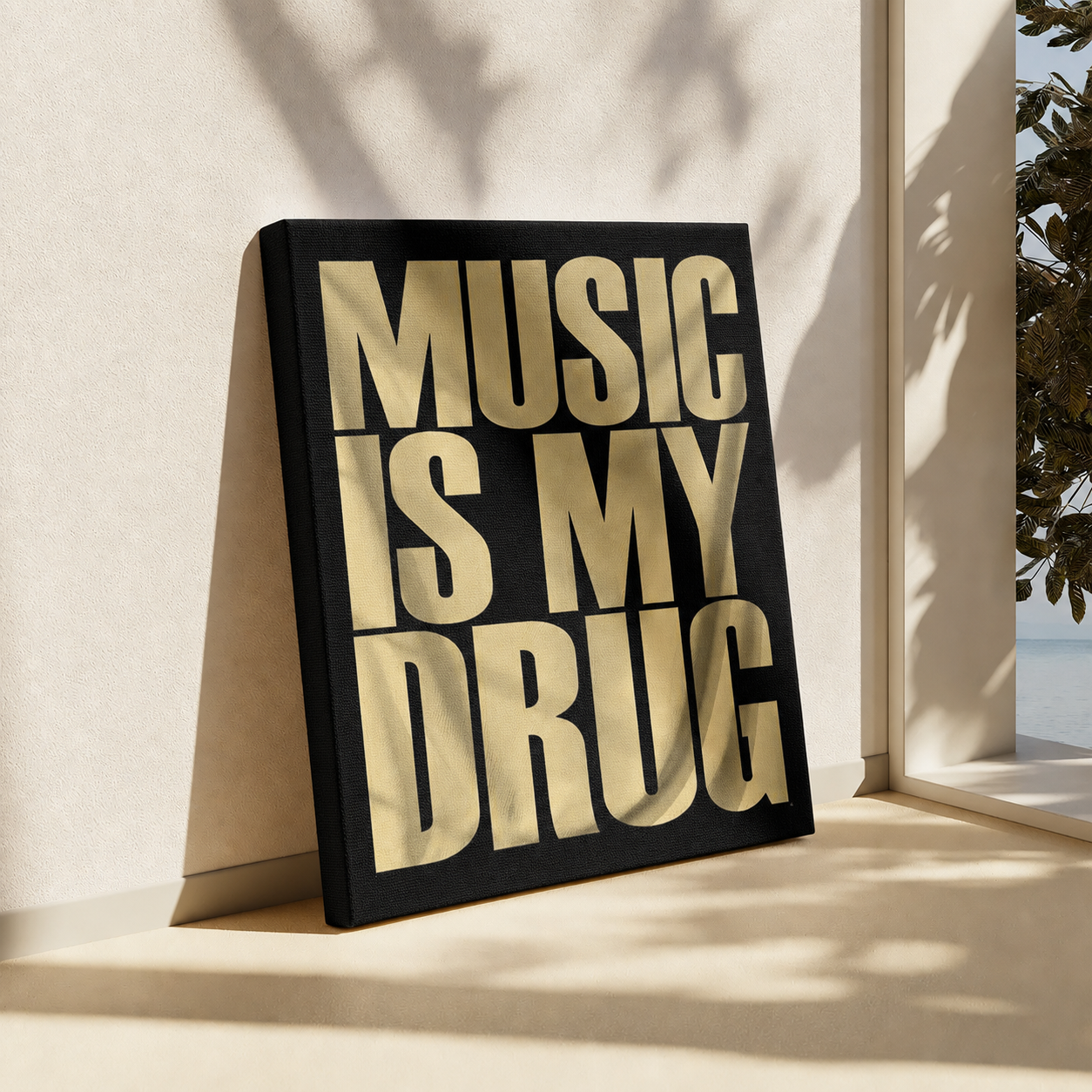 A black canvas wall art print with bold gold lettering that reads 'MUSIC IS MY DRUG', leaning against a beige wall in a sunlit interior near a window.