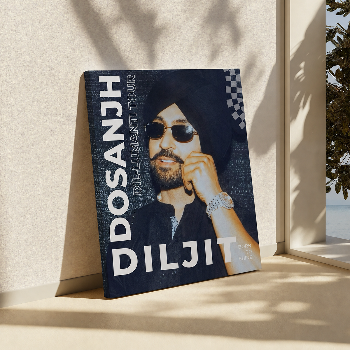 A hardcover book titled 'DOSANJH DILJIT  TOUR' propped up against a beige wall in a sunlit interior corner. The cover features a portrait of a man in a black turban and sunglasses, with large white title text and a dark blue textured background.