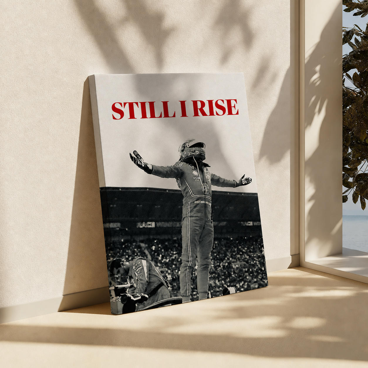 A vertical poster or canvas print leaning against a beige wall on a sunlit surface. The artwork shows a black-and-white racing scene with a driver in a suit and the bold red text 'STILL I RISE' at the top.