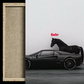 A framed wall art print featuring a black sports car with a black horse on top, set against a light gray background with the red text 'Sabr' above the car. The left side shows a close-up of the textured beige mat board and light wood frame.