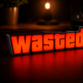 A 3D block-style sign spelling 'Wasted' in glowing orange-red letters on a black base, placed on a dark wooden surface with a warm blurred background.