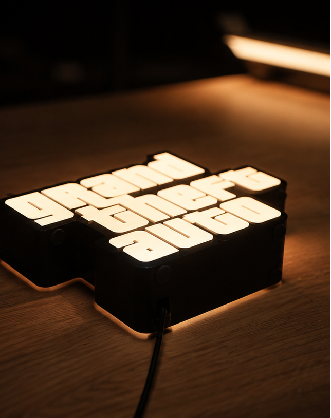 A black LED light sign spelling out 'Grand Theft Auto' in illuminated letters, placed on a wooden surface with warm ambient lighting.
