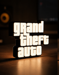 A 3D LED light sign featuring the 'Grand Theft Auto' logo, glowing with a warm white light against a dark background.