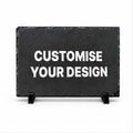 A rectangular black slate sign on small black display stands with the words 'CUSTOMISE YOUR DESIGN' in large white capital letters, shown on a plain white background.