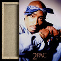 A framed art print featuring a portrait of 2 Pac with a blue bandana and light blue shirt, shown next to a textured beige mat board with a light wood frame.