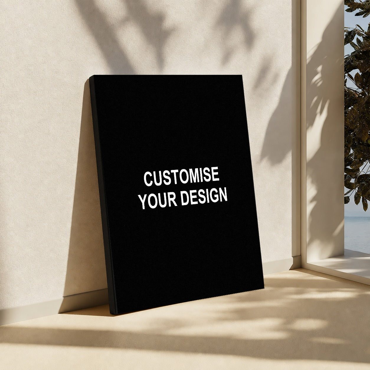 A black rectangular sign or poster leaning against a beige wall in a sunlit interior. The front has the words 'CUSTOMISE YOUR DESIGN' in white uppercase text.