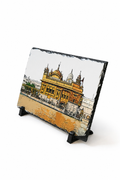 A rectangular slate serving board featuring a hand-painted illustration of the Golden Temple in Amritsar, displayed on a black stand against a white background.