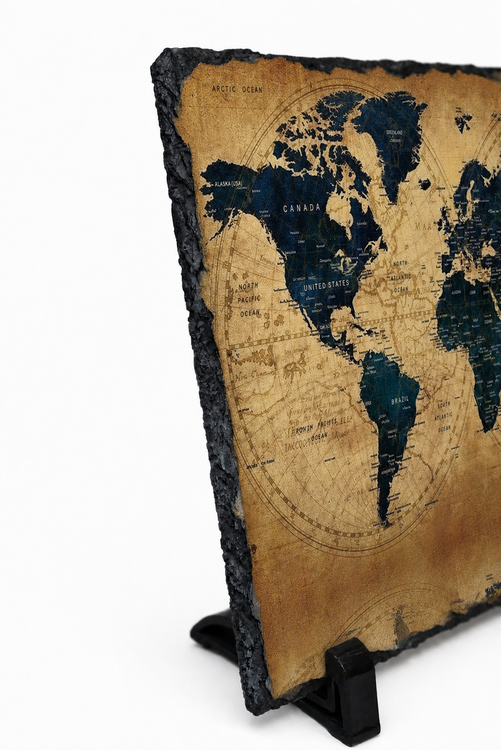 A rectangular slate world map plaque with a rustic dark gray stone edge and a tan parchment-style map surface, displayed on a small black stand against a white background.