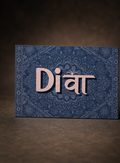 A rectangular blue decorative card or box with an ornate floral pattern and the word 'Divi' in large metallic pink letters, photographed against a dark brown textured background.