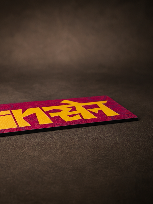 A rectangular card or plaque with bold yellow  text on a textured magenta background, photographed on a dark brown surface.